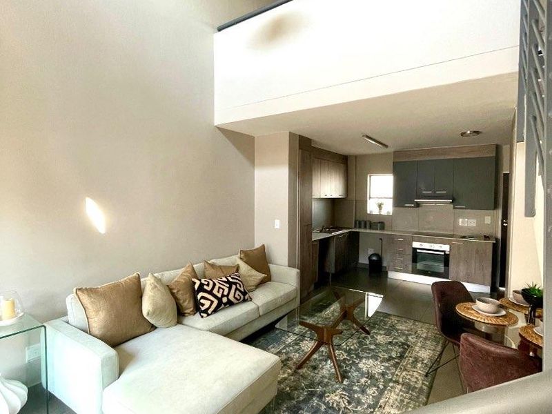 Modern open-plan living area featuring a double-volume ceiling, mezzanine level, and a well-appointed kitchen with built-in cabinetry and appliances.