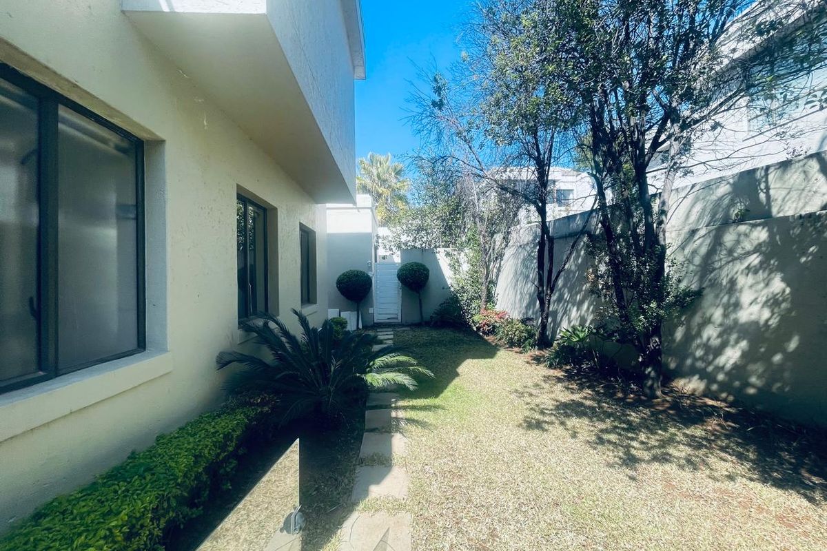 A private rear garden area featuring a paved walkway, established trees, and a secure boundary wall, providing a quiet outdoor space.
