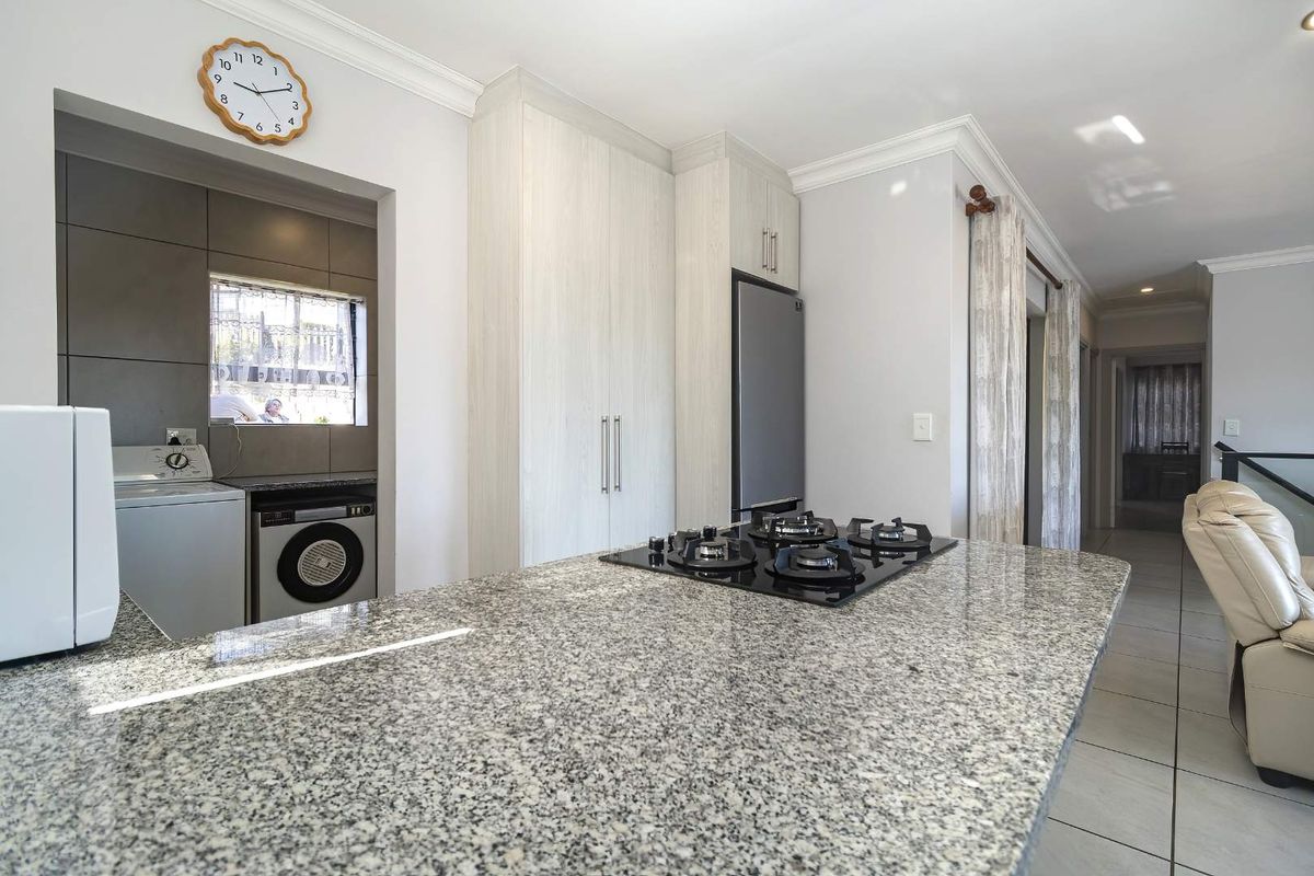 Modern kitchen featuring a granite island with a gas hob, ample built-in cabinetry, and an adjacent scullery area with tiled flooring.