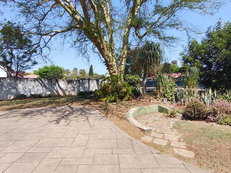 A spacious garden area featuring a paved patio, stone pathway, mature tree, and perimeter wall, offering a private outdoor space.