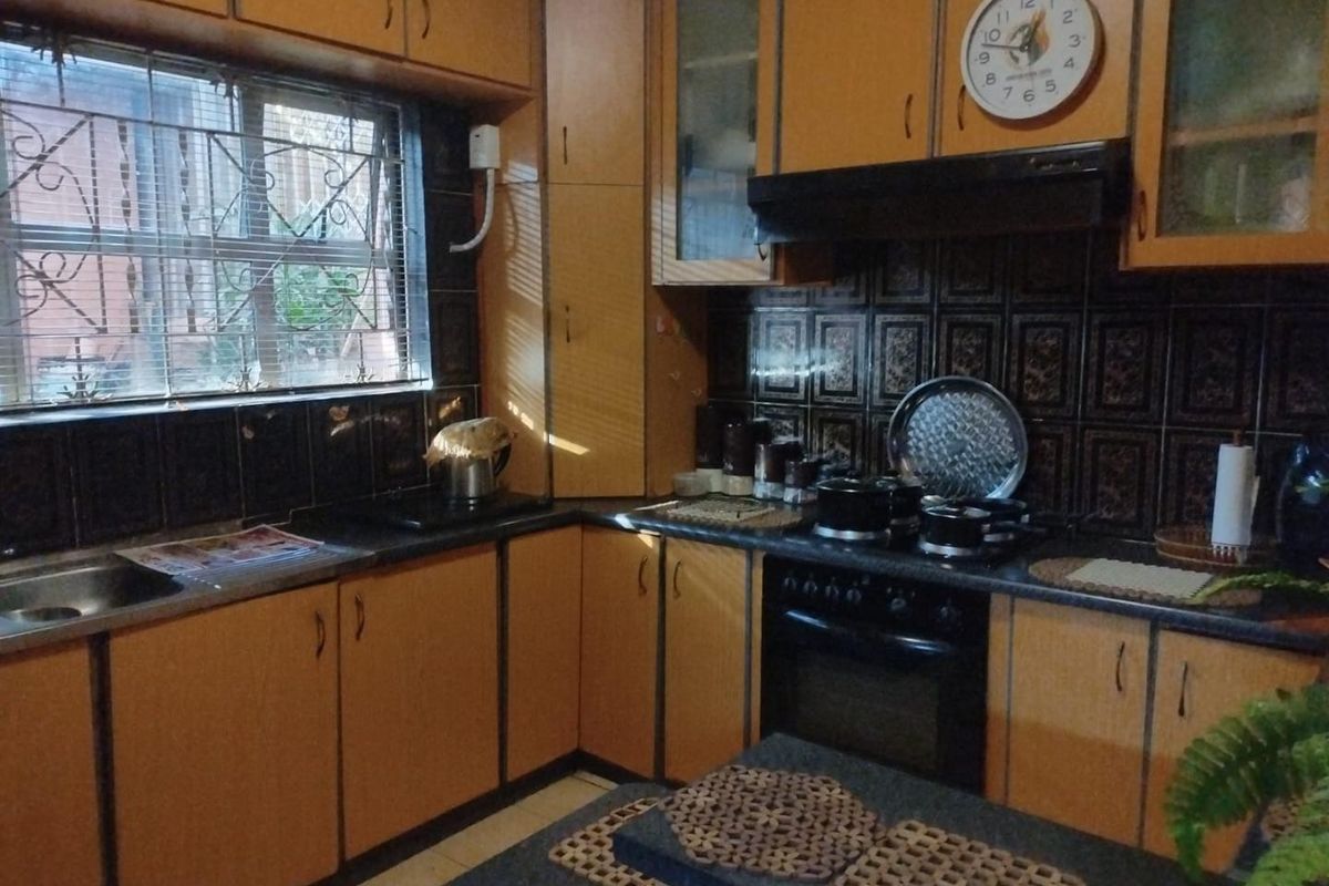 A functional kitchen featuring wood-tone cabinetry, dark tiled backsplash, built-in oven, extractor fan, and a stainless steel sink with security-barred window.