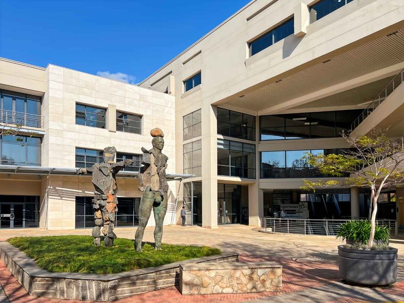 A modern office building exterior featuring a paved courtyard, stone-clad facade, and large glass windows, creating a professional and well-maintained corporate environment.