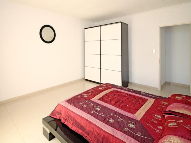 A spacious bedroom featuring neutral tiled flooring and a built-in wardrobe, offering a clean and functional living space.