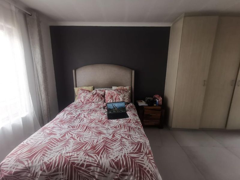 A functional bedroom featuring neutral tiled flooring, a dark accent wall, and built-in cupboards providing ample storage space.