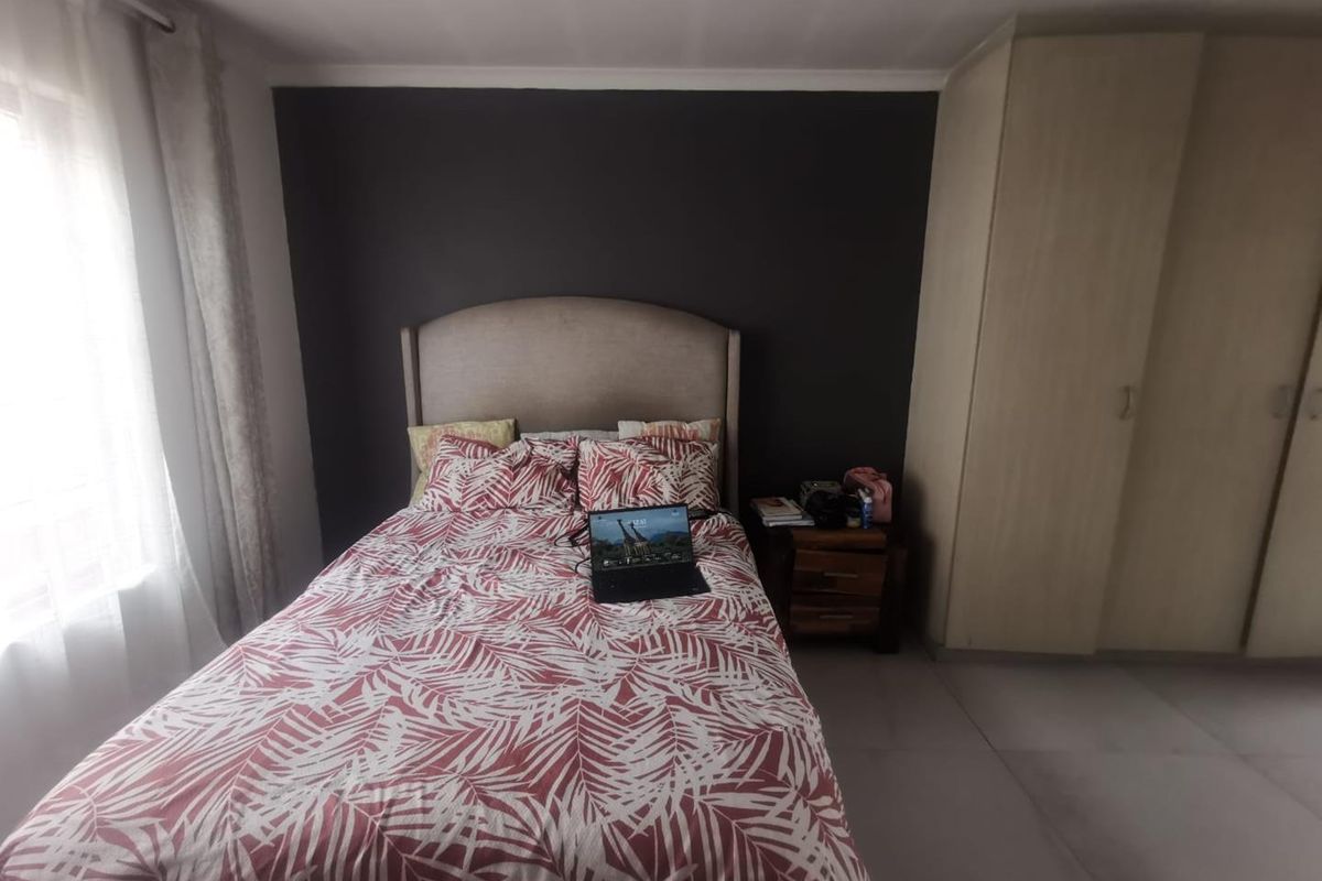 A functional bedroom featuring neutral tiled flooring, a dark accent wall, and built-in cupboards providing ample storage space.