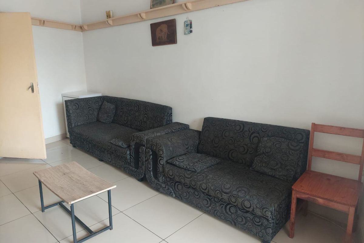 A living room area featuring tiled flooring and a wall-mounted wooden display shelf.