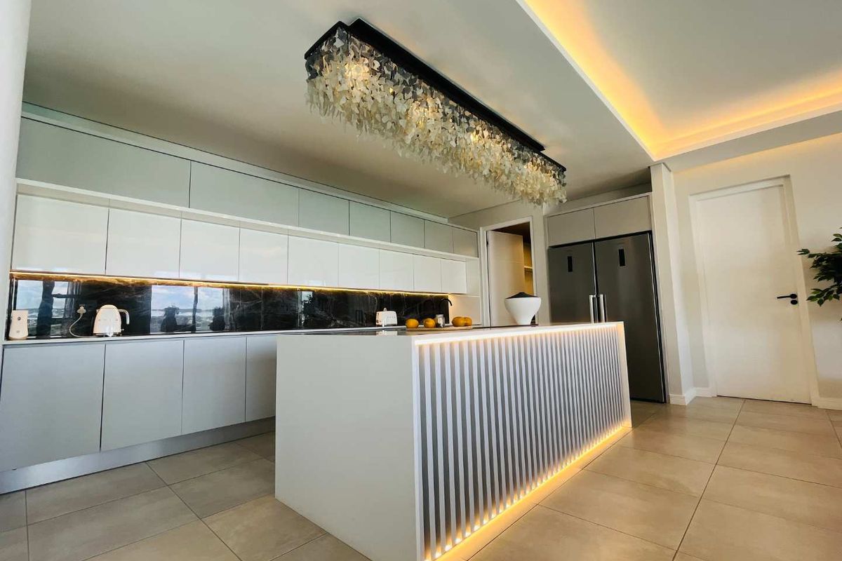 Modern luxury kitchen featuring a central island with integrated LED lighting, sleek handleless cabinetry, dark stone splashback, and a statement decorative pendant light.