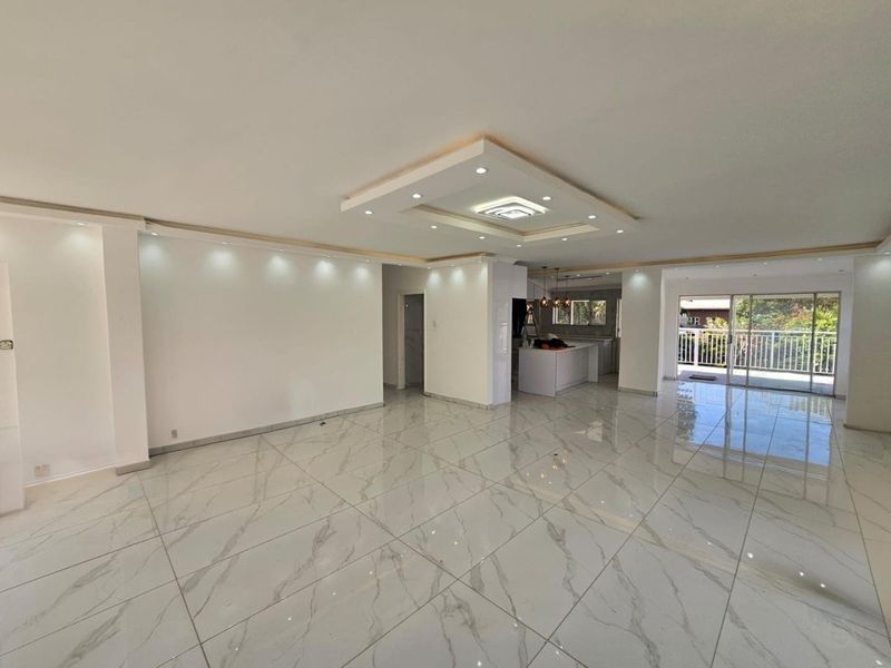 Spacious open-plan living area featuring polished marble-look floor tiles, a modern coffered ceiling with recessed lighting, and seamless access to an outdoor balcony.