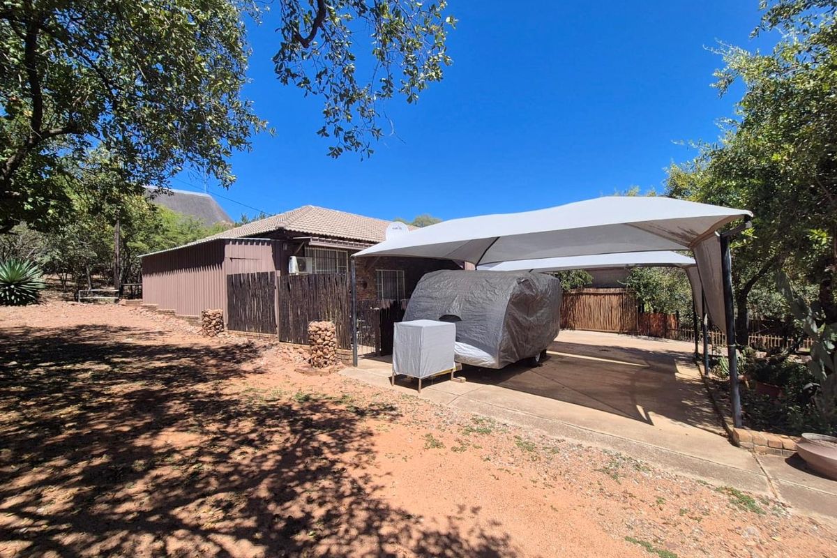 Exterior view of the property featuring a paved driveway, a covered carport structure, and established surrounding trees.