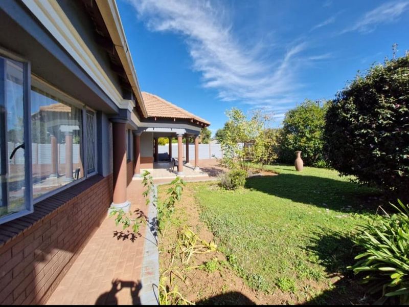 A view of the rear garden featuring a covered patio area with brick paving, columns, and a well-maintained lawn.