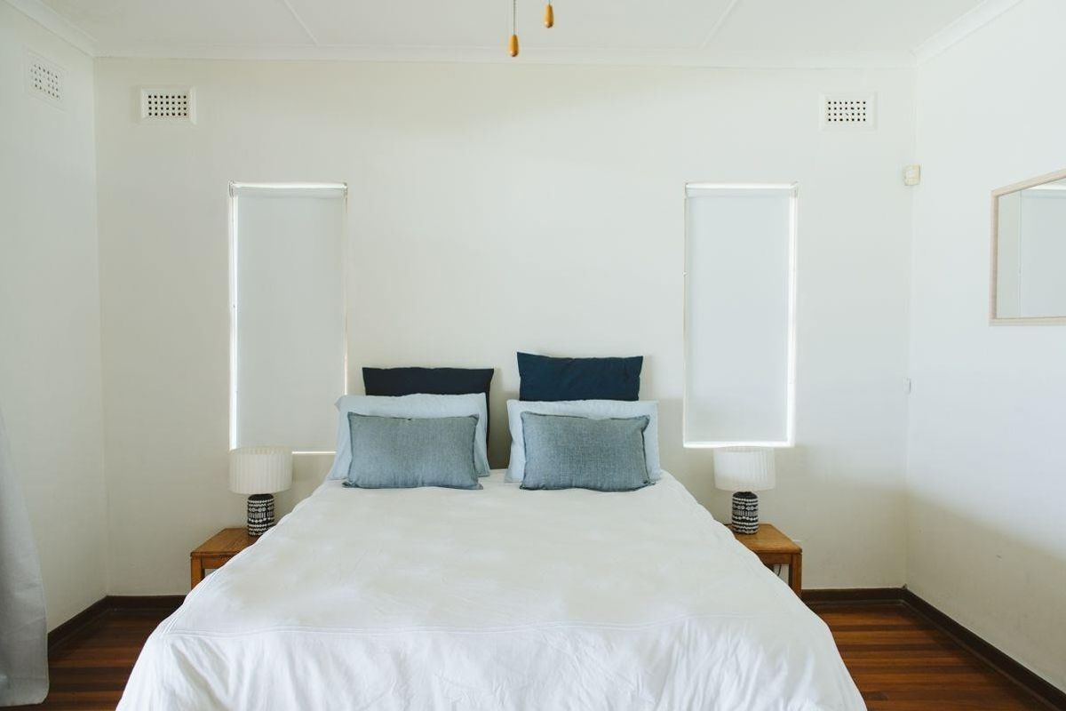 A bright and well-maintained bedroom featuring polished hardwood flooring, dual windows with roller blinds, and a ceiling fan.