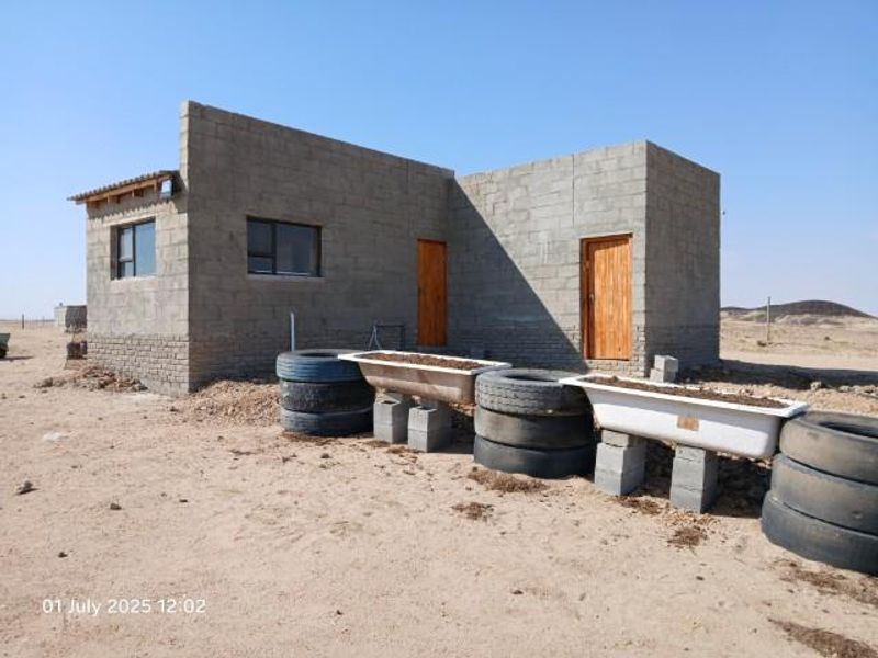 An unfinished small holding structure featuring exposed concrete block walls, timber doors, and aluminium window frames, set in a rural landscape.