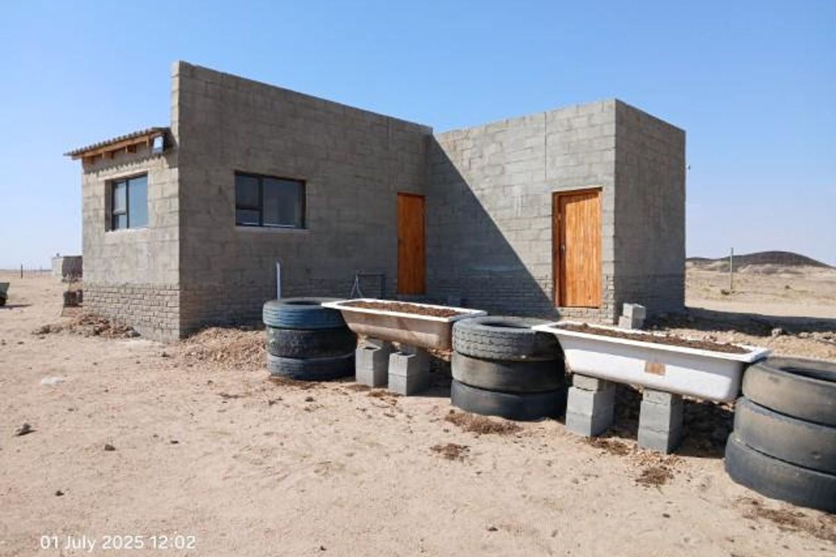 An unfinished small holding structure featuring exposed concrete block walls, timber doors, and aluminium window frames, set in a rural landscape.