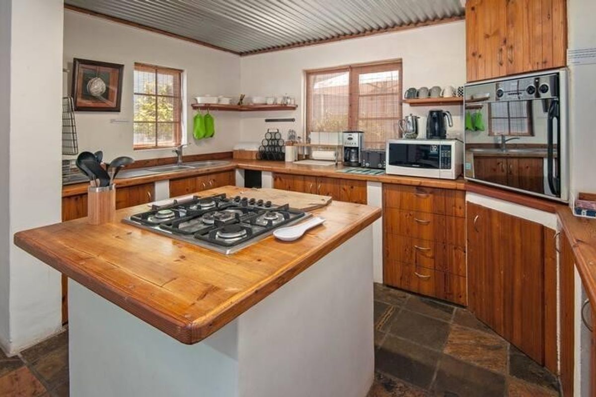 A rustic kitchen featuring a central island with a built-in gas hob, wooden cabinetry, and stone tile flooring under a corrugated metal ceiling.