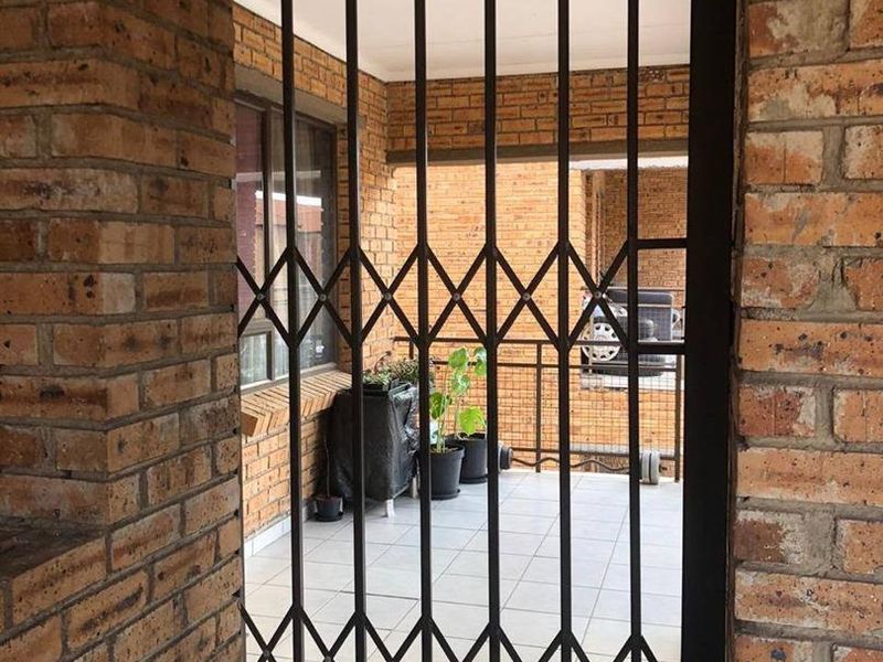 A covered balcony area featuring exposed brick walls, tiled flooring, and a secure metal accordion-style security gate.