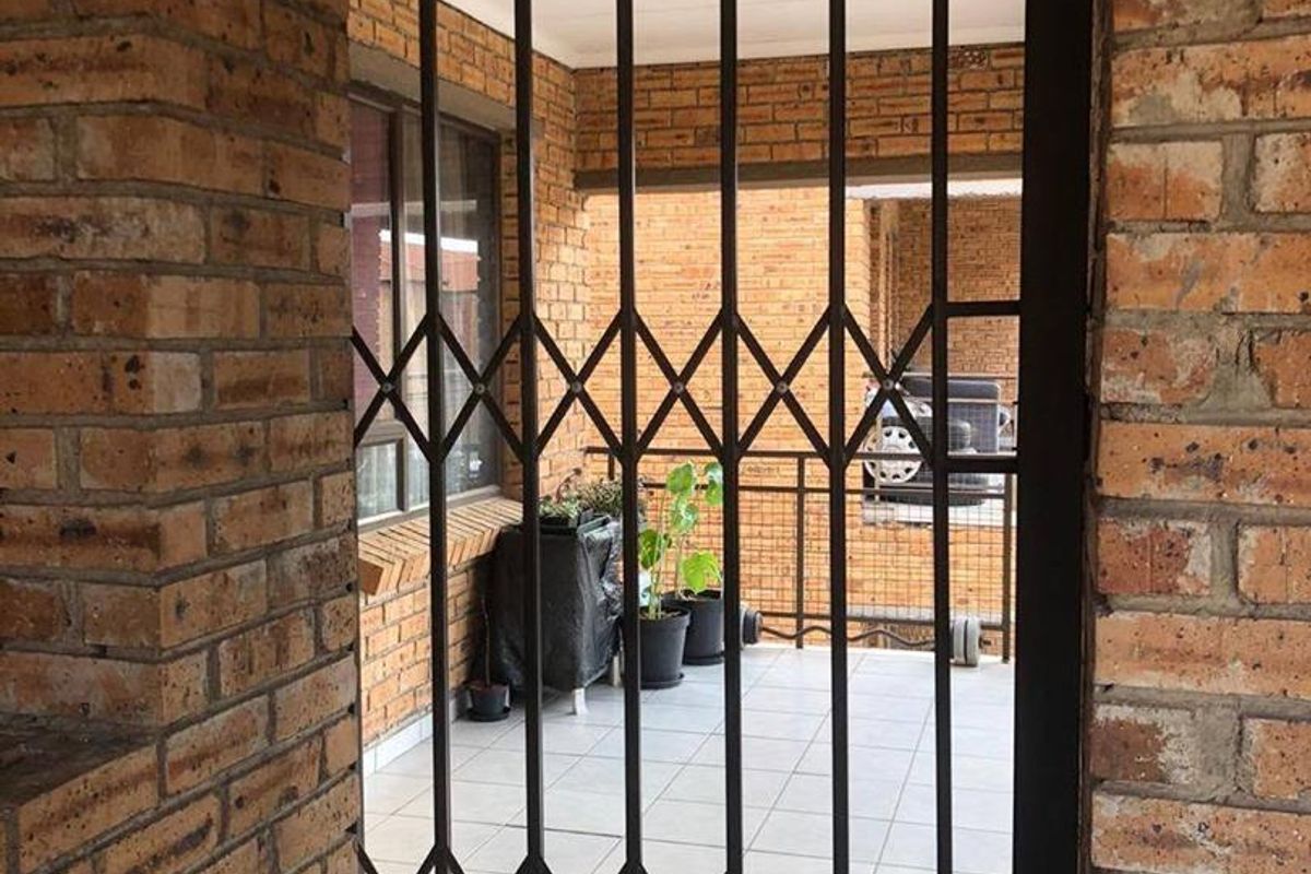 A covered balcony area featuring exposed brick walls, tiled flooring, and a secure metal accordion-style security gate.