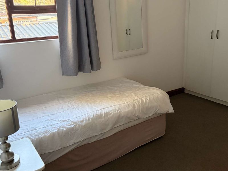 A functional bedroom featuring built-in cupboards, carpeted flooring, and a window providing natural light.
