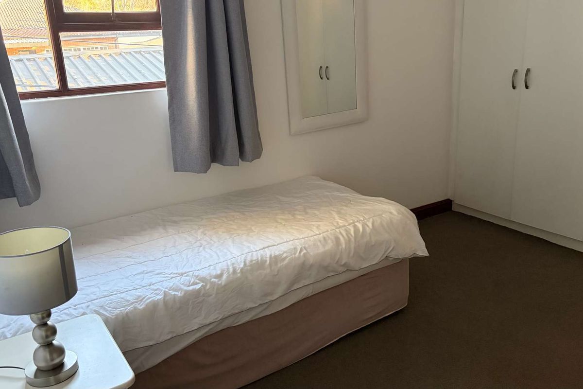 A functional bedroom featuring built-in cupboards, carpeted flooring, and a window providing natural light.