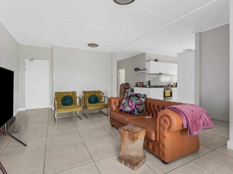 An open-plan living area featuring neutral tiled flooring and a connected kitchen with modern white cabinetry and integrated appliances.