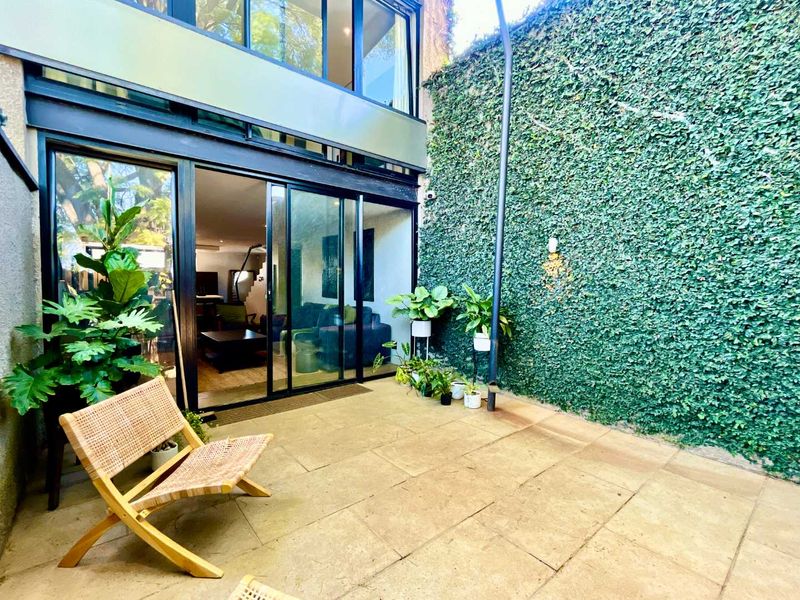 A private paved patio area featuring large sliding glass doors, modern structural beams, and a lush, ivy-covered feature wall.