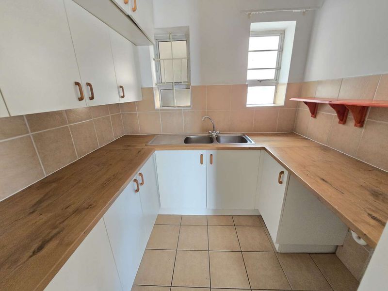 A functional kitchen featuring white cabinetry, wood-look laminate countertops, tiled backsplash, and double bowl sink with natural light from two windows.