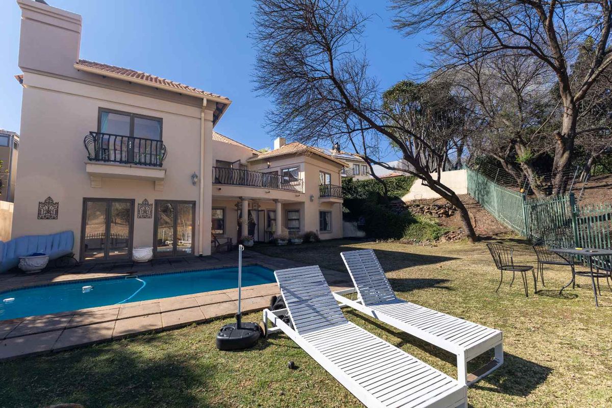 Rear view of the property featuring a swimming pool, paved patio area, and upper-level balconies overlooking the garden.