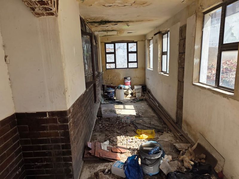 A neglected hallway space featuring brick wall accents and metal-framed windows, currently requiring significant restoration and repair to the ceiling and wall finishes.