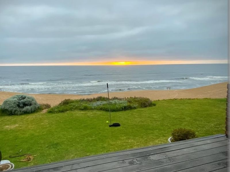 A scenic view of the ocean and beach from a timber deck, featuring a well-maintained lawn area.