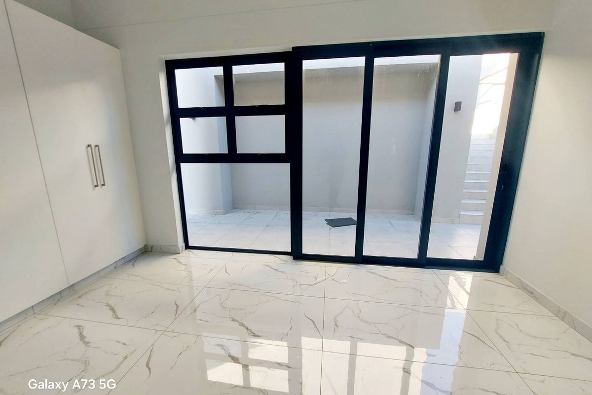 A bright, modern room featuring large black-framed sliding glass doors that open onto a private courtyard, complemented by sleek white built-in cabinetry.