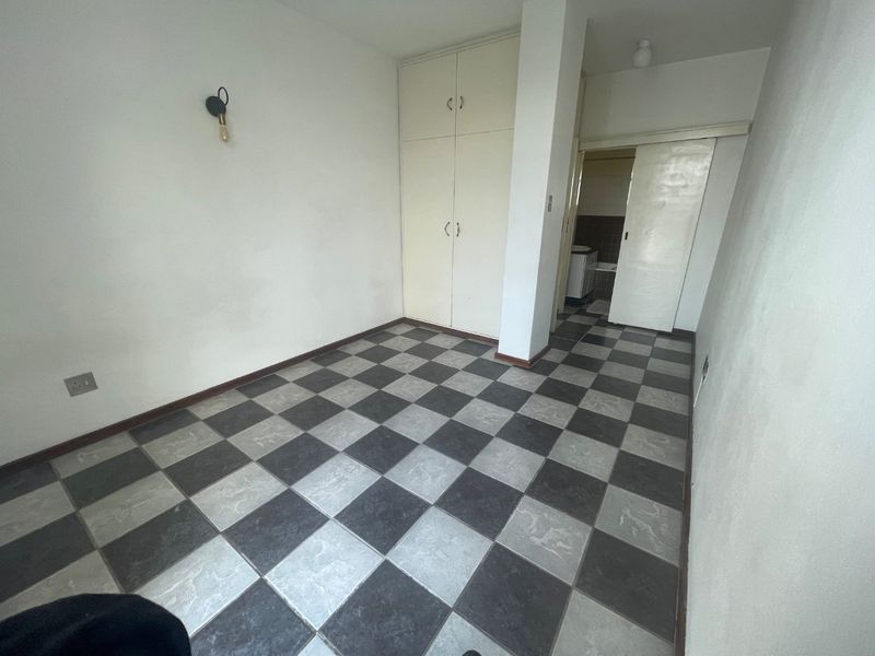 An empty bedroom featuring checkered floor tiles, built-in cupboards, and a sliding door leading to an adjacent room.