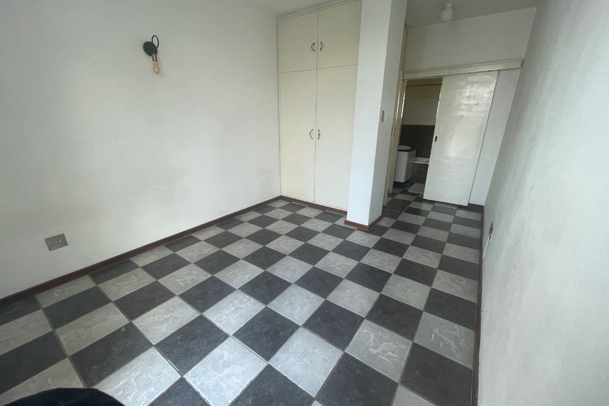 An empty bedroom featuring checkered floor tiles, built-in cupboards, and a sliding door leading to an adjacent room.