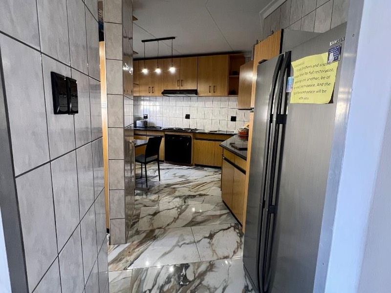 A functional kitchen featuring wooden cabinetry, marble-look tiled flooring, and a tiled splashback, providing a practical workspace with integrated appliances.