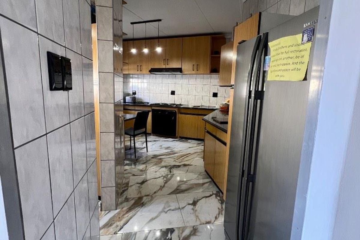 A functional kitchen featuring wooden cabinetry, marble-look tiled flooring, and a tiled splashback, providing a practical workspace with integrated appliances.