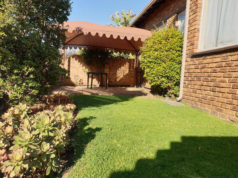 A private rear garden featuring a paved patio area with a fixed fabric gazebo, brick boundary walls, and established lawn.