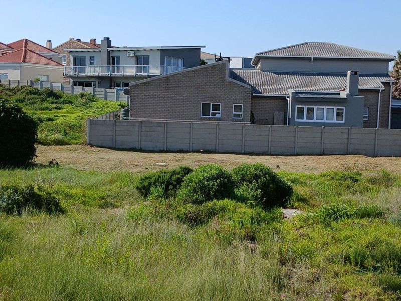 A view of an undeveloped residential plot featuring natural vegetation and a precast concrete boundary wall separating it from neighboring properties.