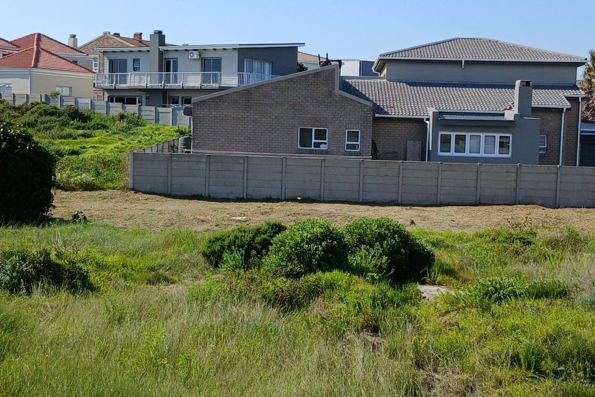 A view of an undeveloped residential plot featuring natural vegetation and a precast concrete boundary wall separating it from neighboring properties.