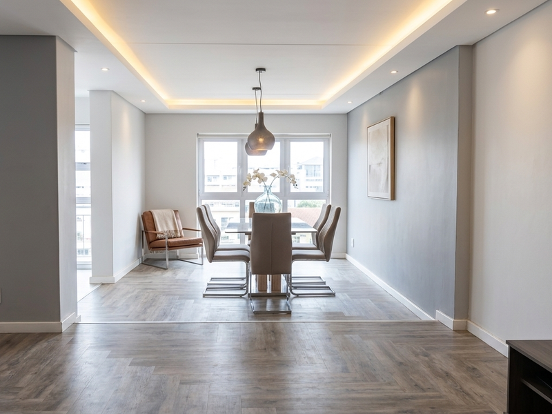 Spacious open-plan living and dining area featuring modern herringbone flooring, recessed cove lighting, and large windows providing ample natural light.