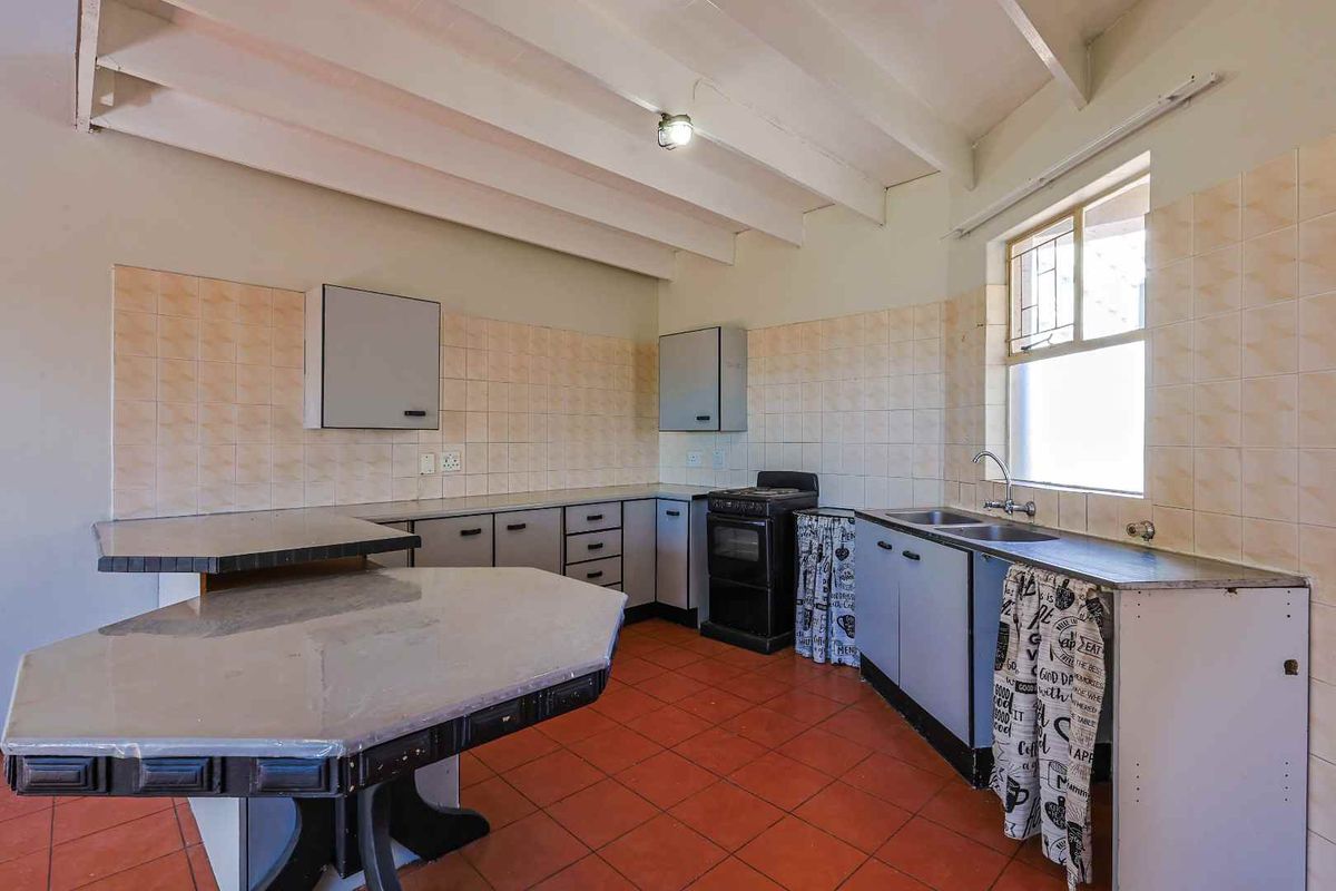 A dated kitchen featuring tiled flooring, a tiled backsplash, built-in cabinetry, a double sink, and a freestanding stove.