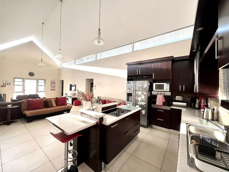 Spacious open-plan living area featuring a modern kitchen with dark cabinetry, a central island, vaulted ceilings, and abundant natural light from clerestory windows.