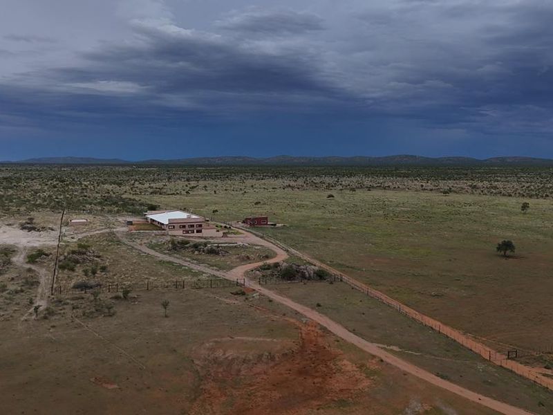 An aerial view of a rural farm property featuring a main dwelling, outbuildings, and extensive surrounding land under a dramatic cloudy sky.