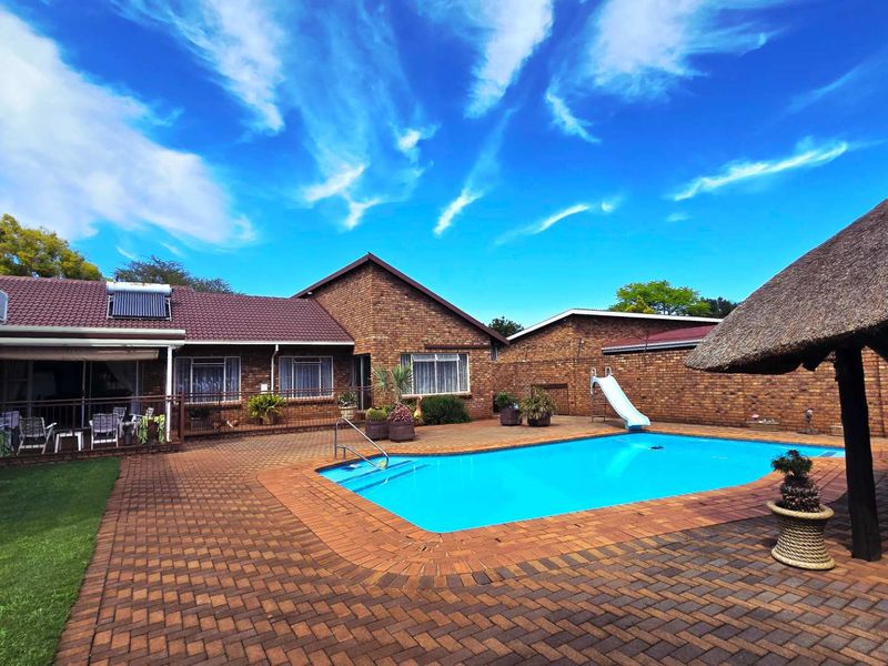 Spacious outdoor entertainment area featuring a swimming pool with a slide, brick paving, and a traditional thatched lapa structure.