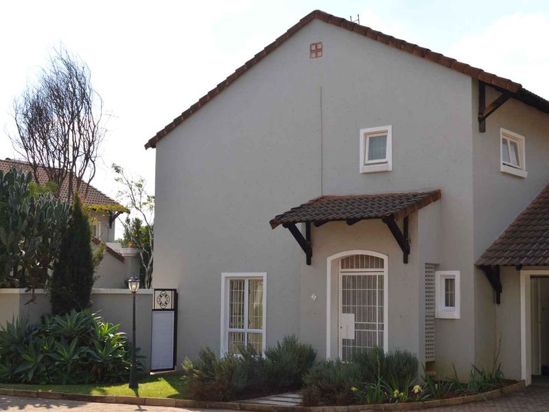 Front elevation of a residential house featuring a tiled roof, security gate, and landscaped garden area with a paved driveway.
