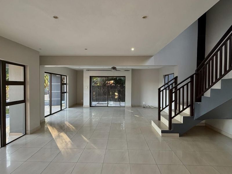Spacious open-plan living area featuring neutral tiled flooring, recessed lighting, a central staircase, and large sliding glass doors providing access to the outdoor area.