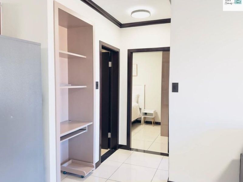 A clean, well-lit hallway featuring tiled flooring, dark trim accents, and a built-in shelving unit, providing access to adjacent rooms.