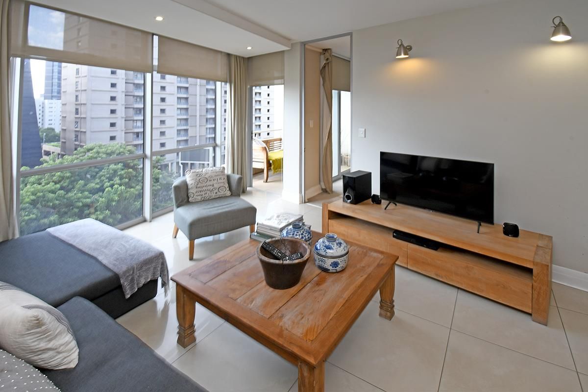 A bright, modern living room featuring large floor-to-ceiling windows, tiled flooring, and recessed ceiling lighting with access to an adjoining balcony.