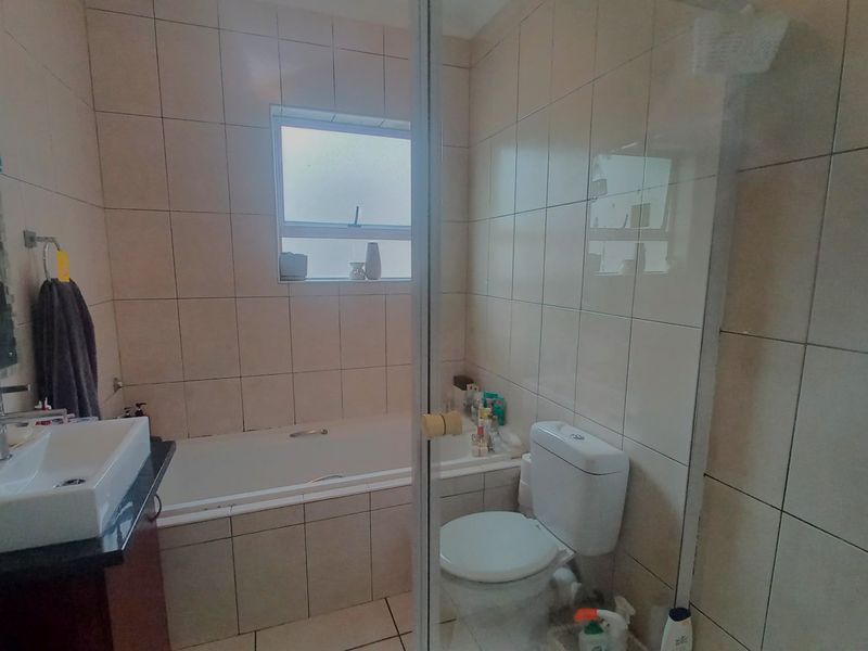 A functional bathroom featuring a built-in bathtub, wall-mounted basin with vanity, toilet, and tiled finishes throughout.
