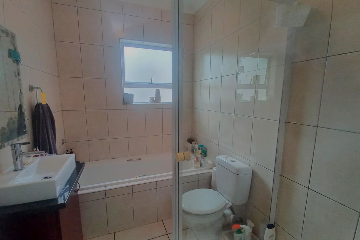 A functional bathroom featuring a built-in bathtub, wall-mounted basin with vanity, toilet, and tiled finishes throughout.