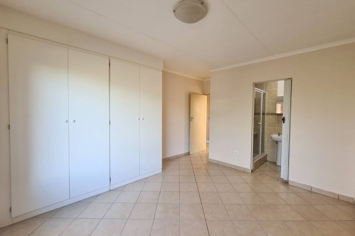 A spacious, empty bedroom featuring neutral tiled flooring, ample built-in cupboard storage, and direct access to an en-suite bathroom.