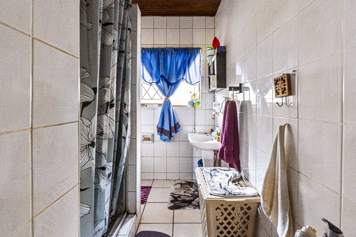A functional bathroom featuring a pedestal basin, shower enclosure, and full-height ceramic wall tiling, presenting an opportunity for modern cosmetic updates.