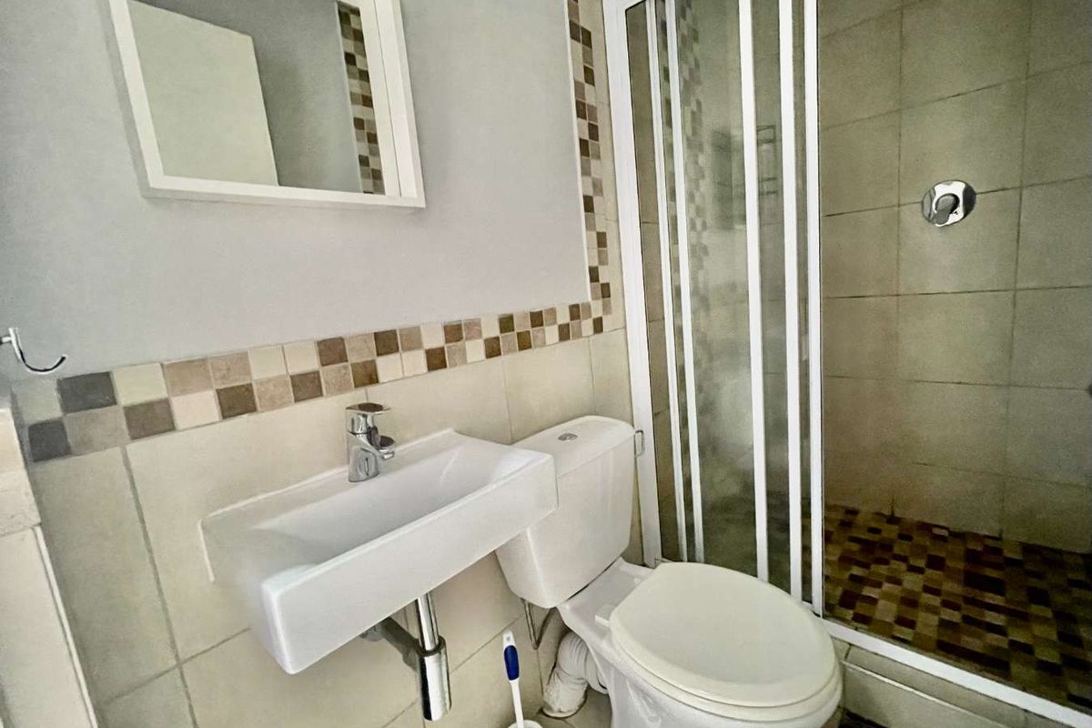 Compact bathroom featuring a wall-mounted basin, toilet, and a tiled shower enclosure with a sliding door.